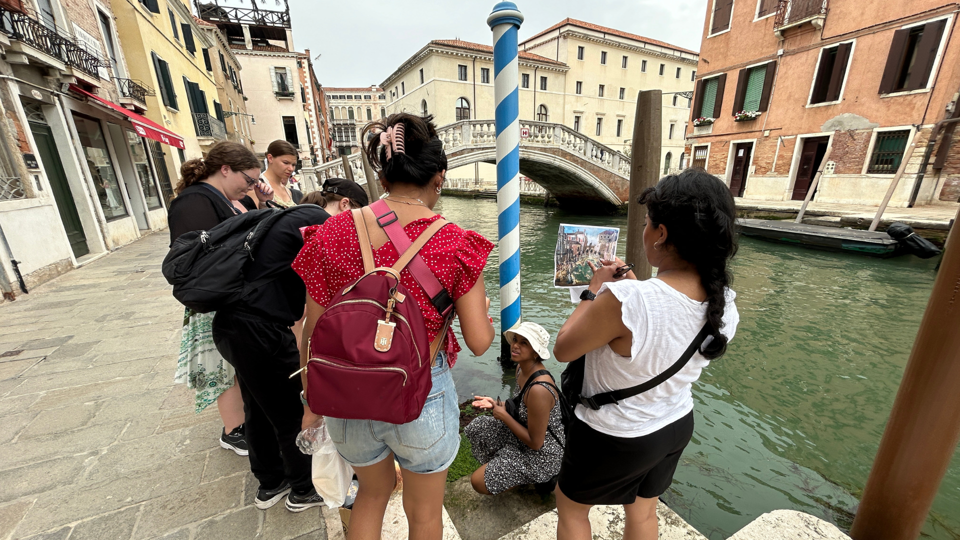 Two students looking out at a canal in Venice. They are holding up an older image of Venice to compare the water levels. 