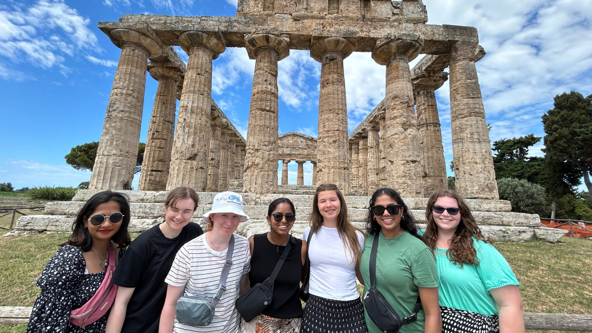 Seven students standing in front on ancient ruins in Italy. 