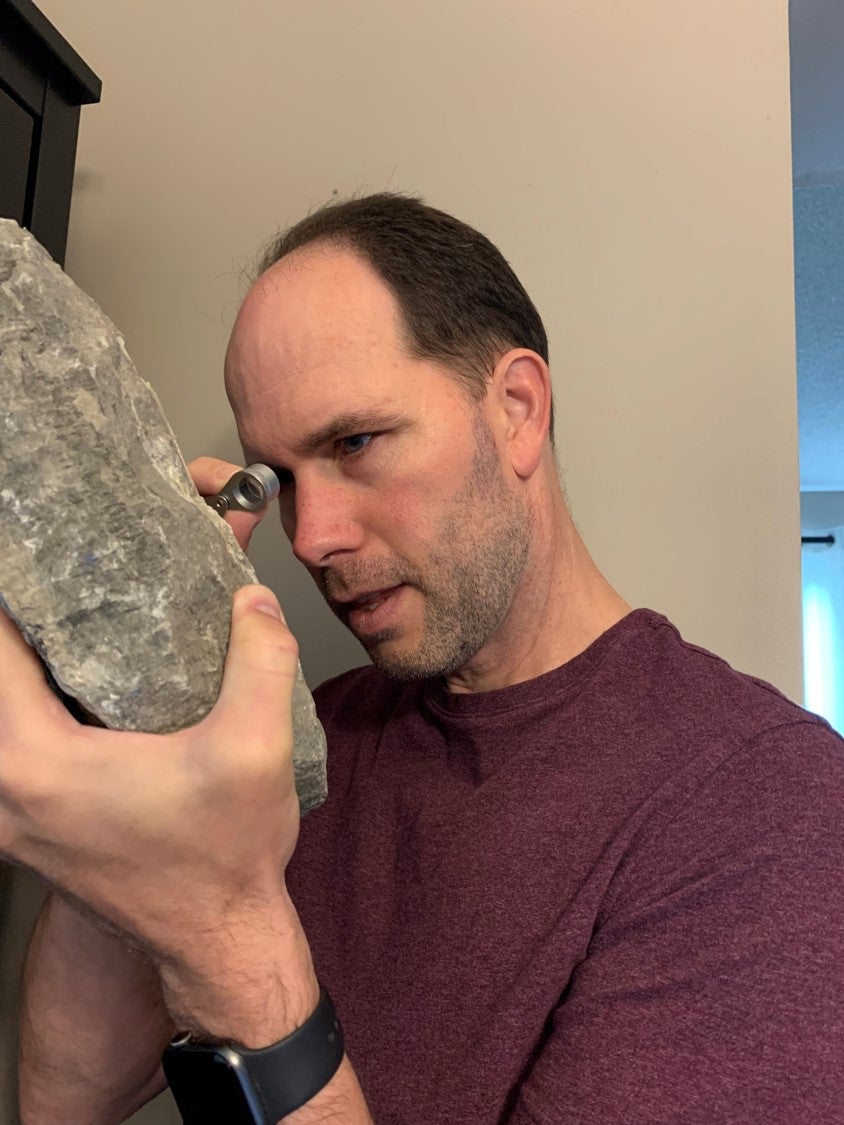 John Johnston looking at a large rock with a hand lens.