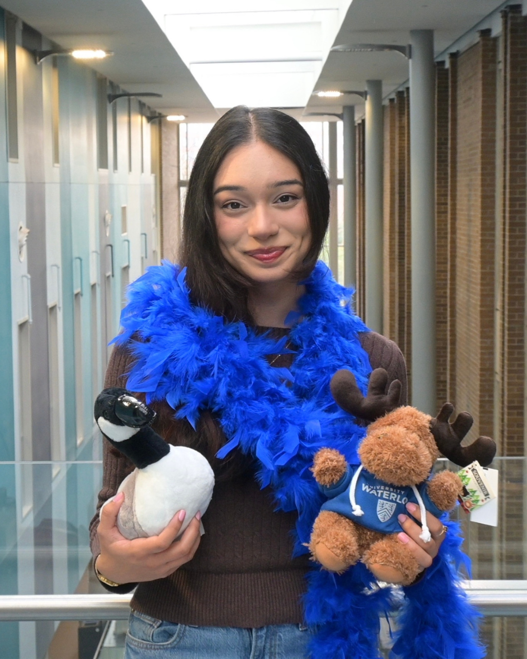 Mona in the Science Teaching Complex wearing a blue feather boa and holding a goose and moose stuffed animal.