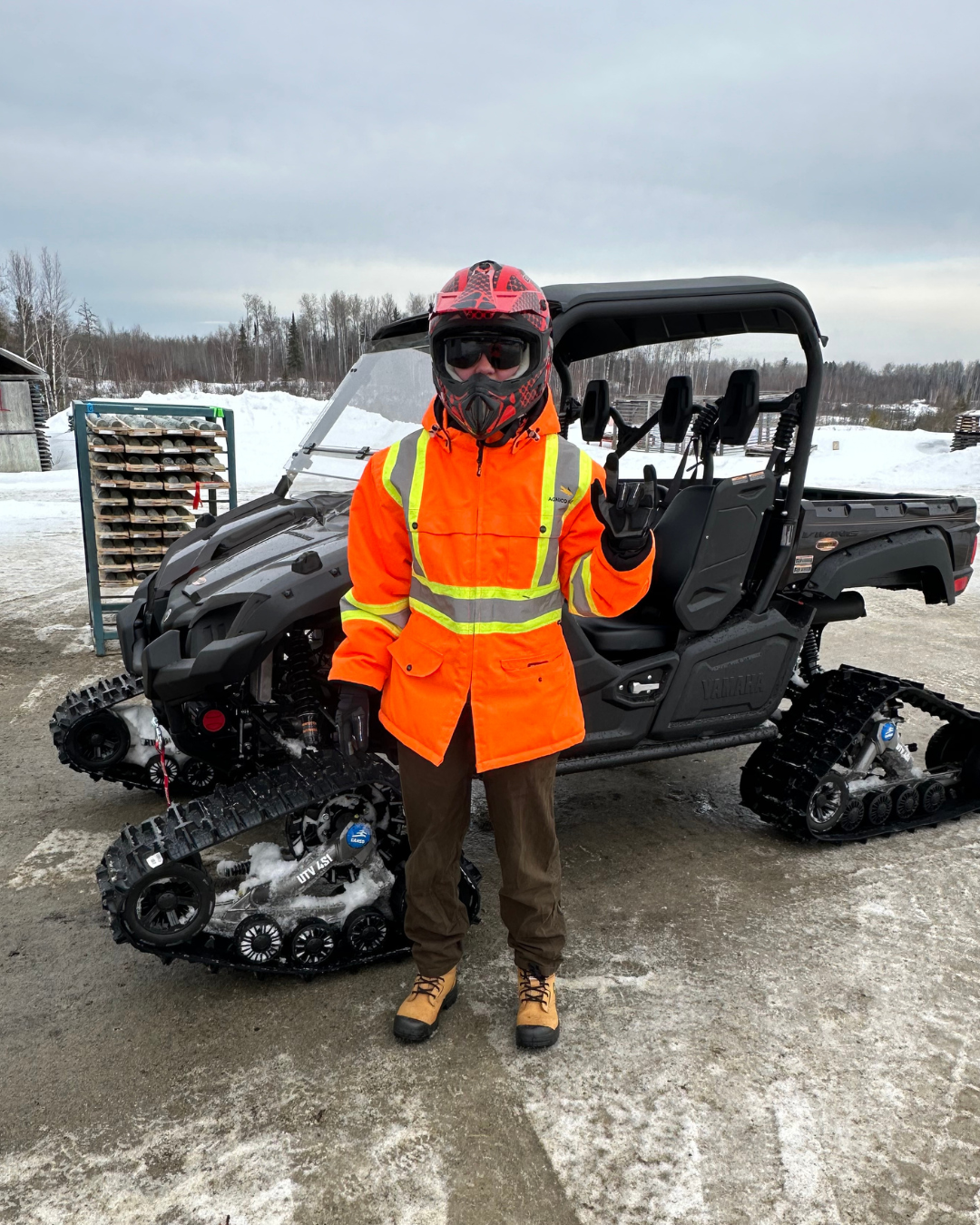 Nathalie wearing an orange safety coat standing in front of an ATV in the winter.
