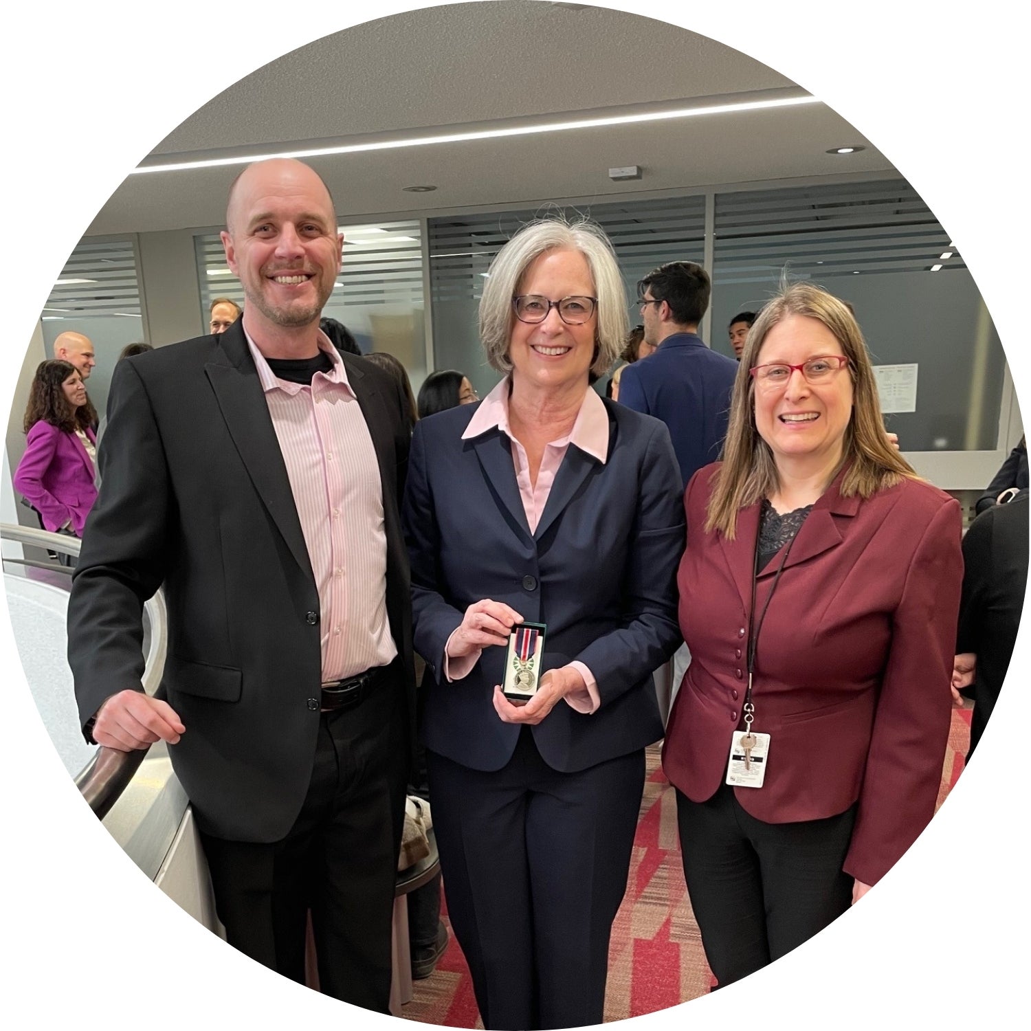 Pat Rasmussen holding a medal, standing beside her award nominators