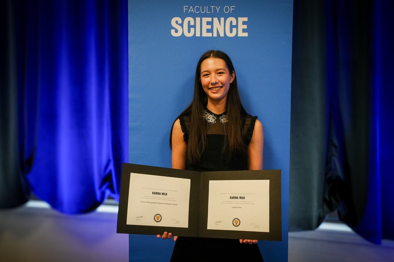 A student standing against a blue background that says "science". The student is holder a certificate award. 