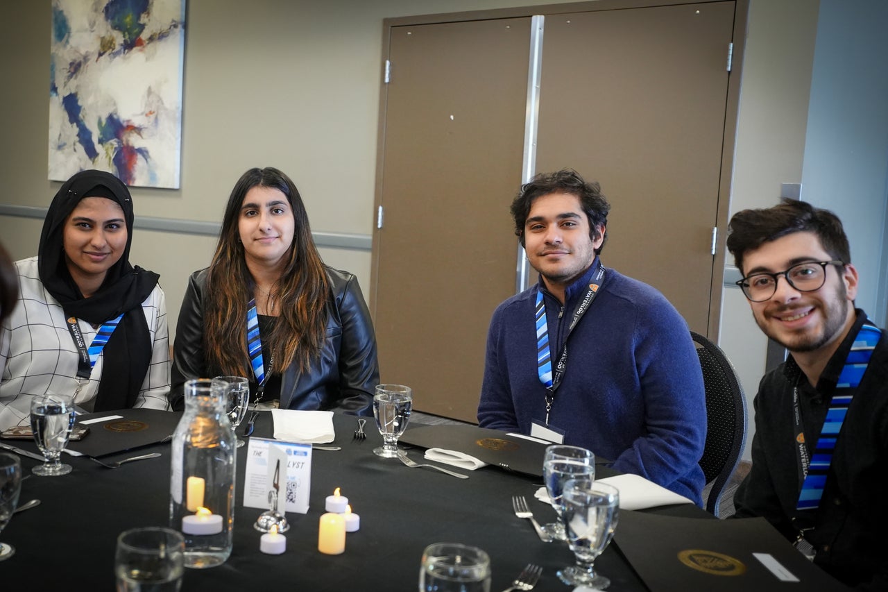 Four students wearing blue science lanyards in a banquet hall.