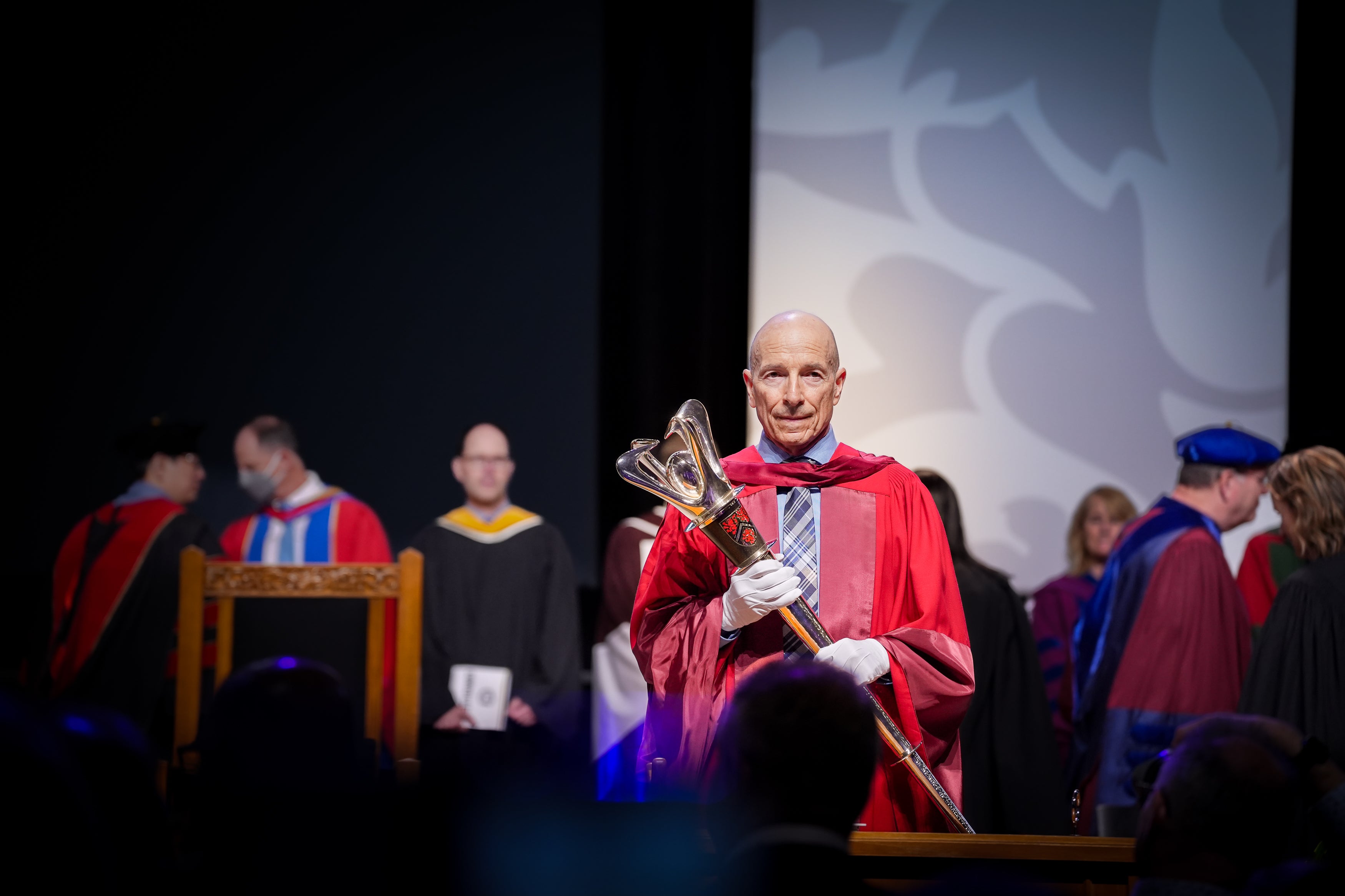Mario Coniglio stands on the stage holding the mase at the the Spring 2025 convocation. 