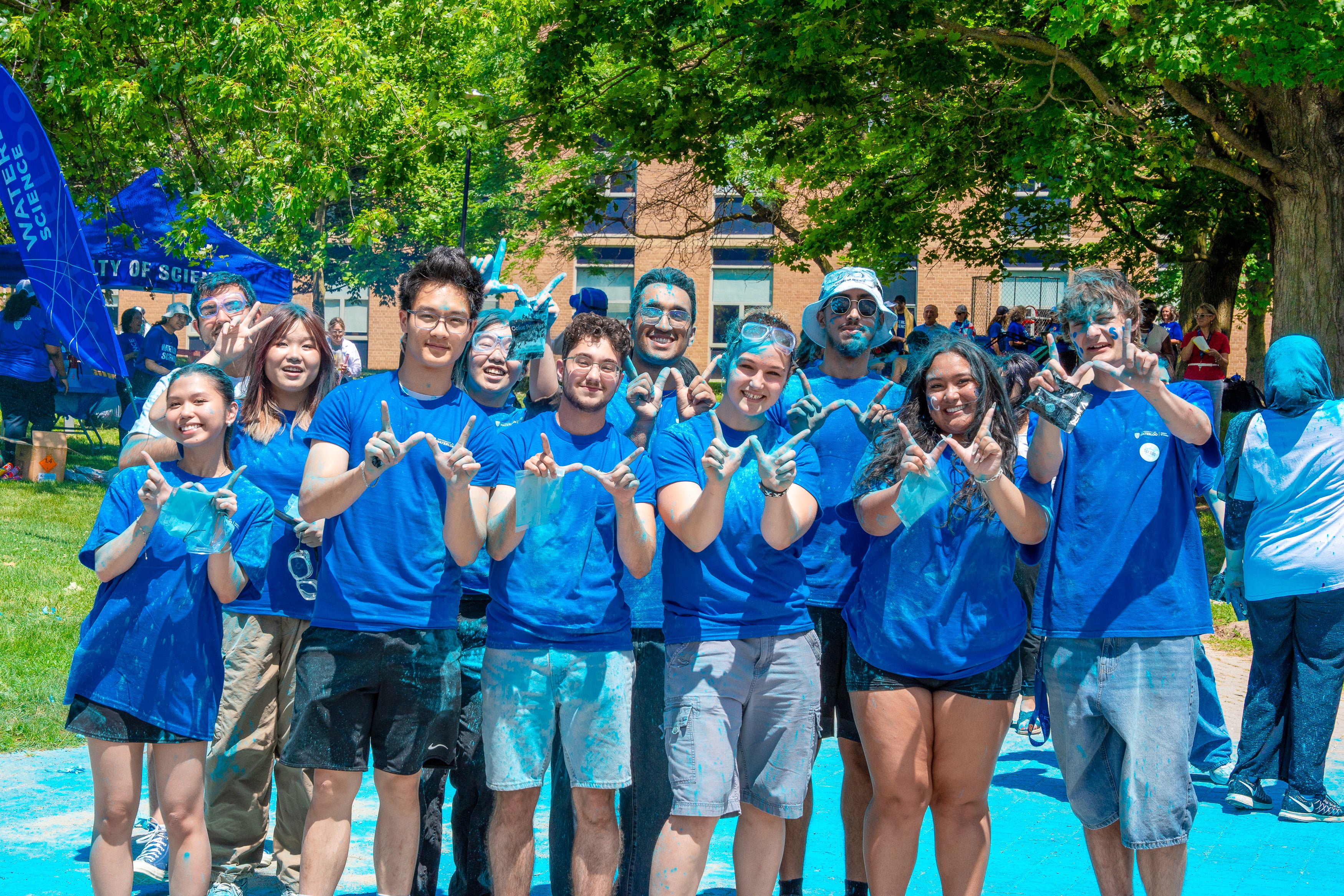 A group of students dyed blue, smiling and holding up a W shape with their fingers