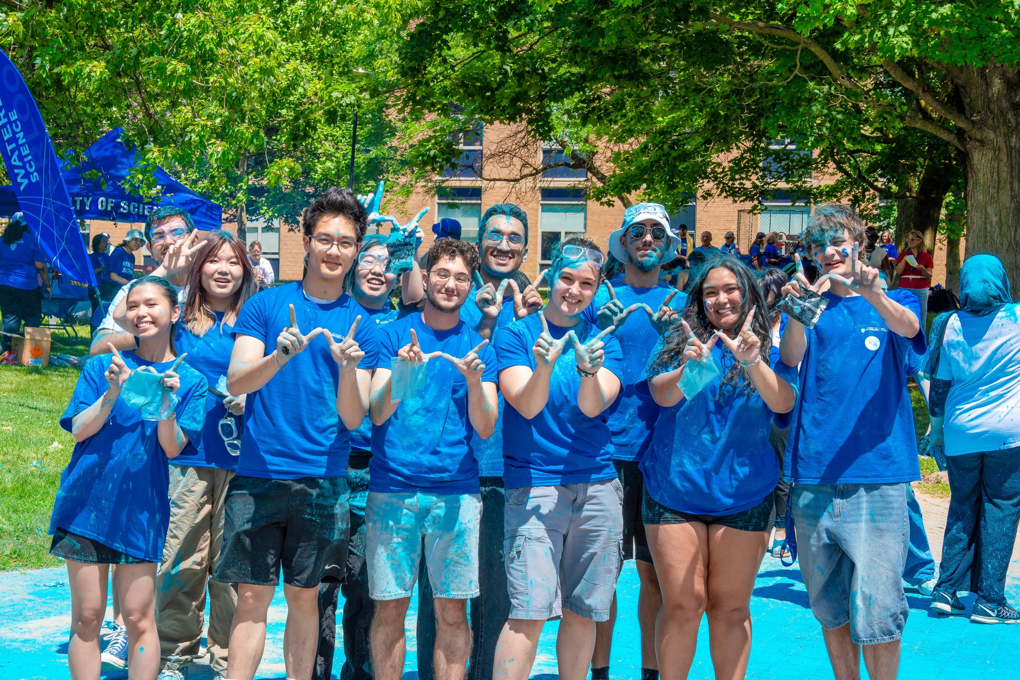 A group of students dyed blue, smiling and holding up a W shape with their fingers