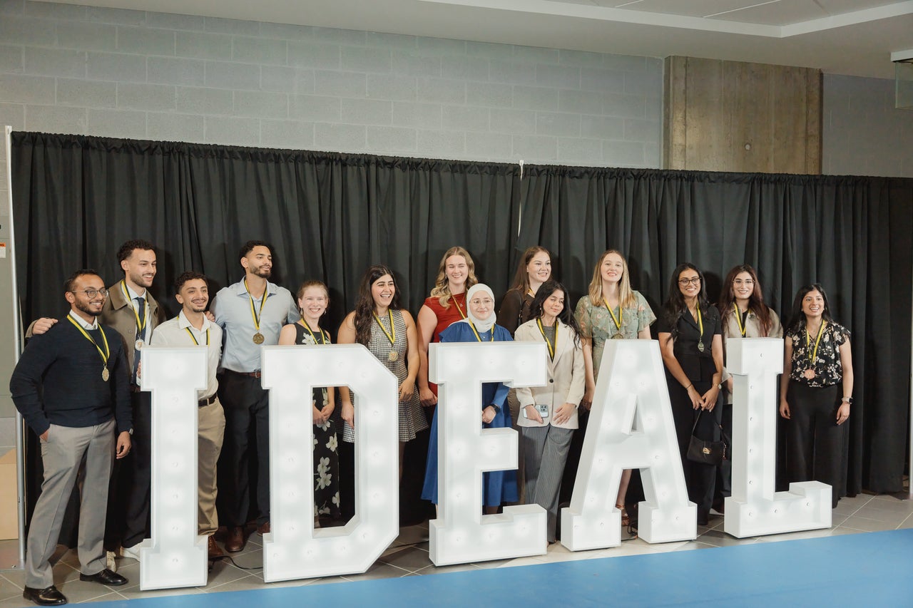 Medal winners standing behind large letters that spell "IDEAL"