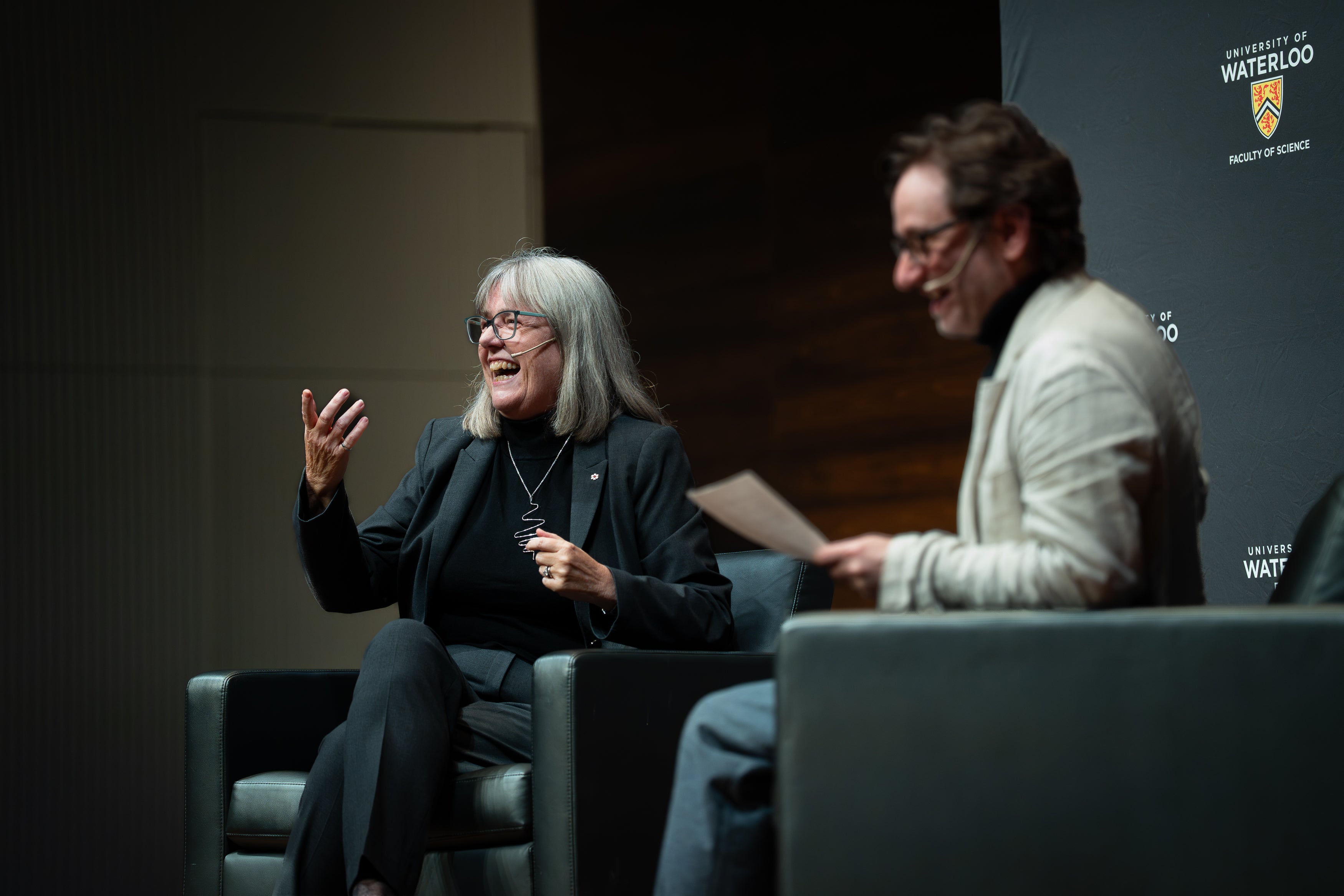 Donna Strickland and Joe Sanderson on chairs on a stage
