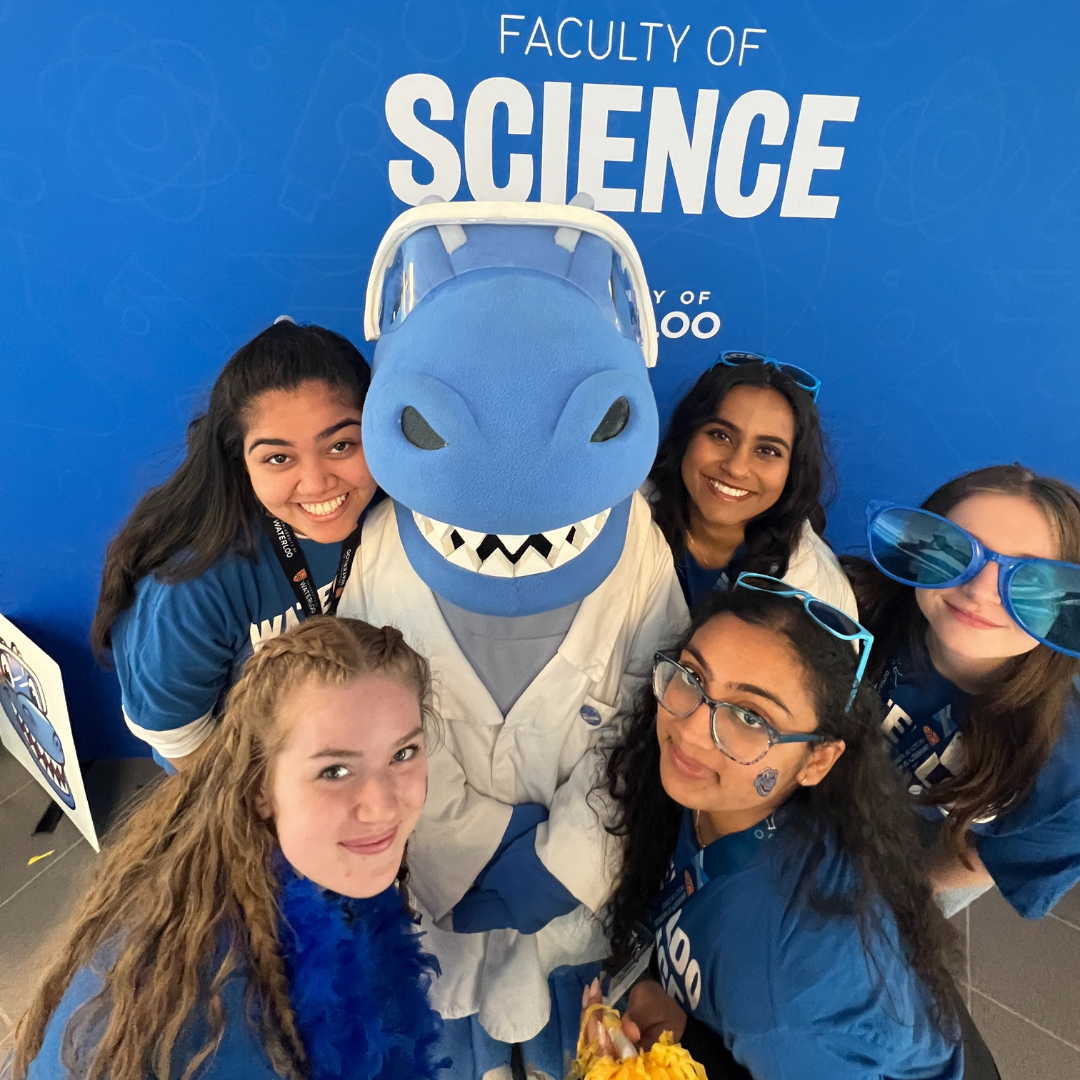 Five students standing in front of a blue Faculty of Science sign with Cobalt (a blue dinosaur mascot)