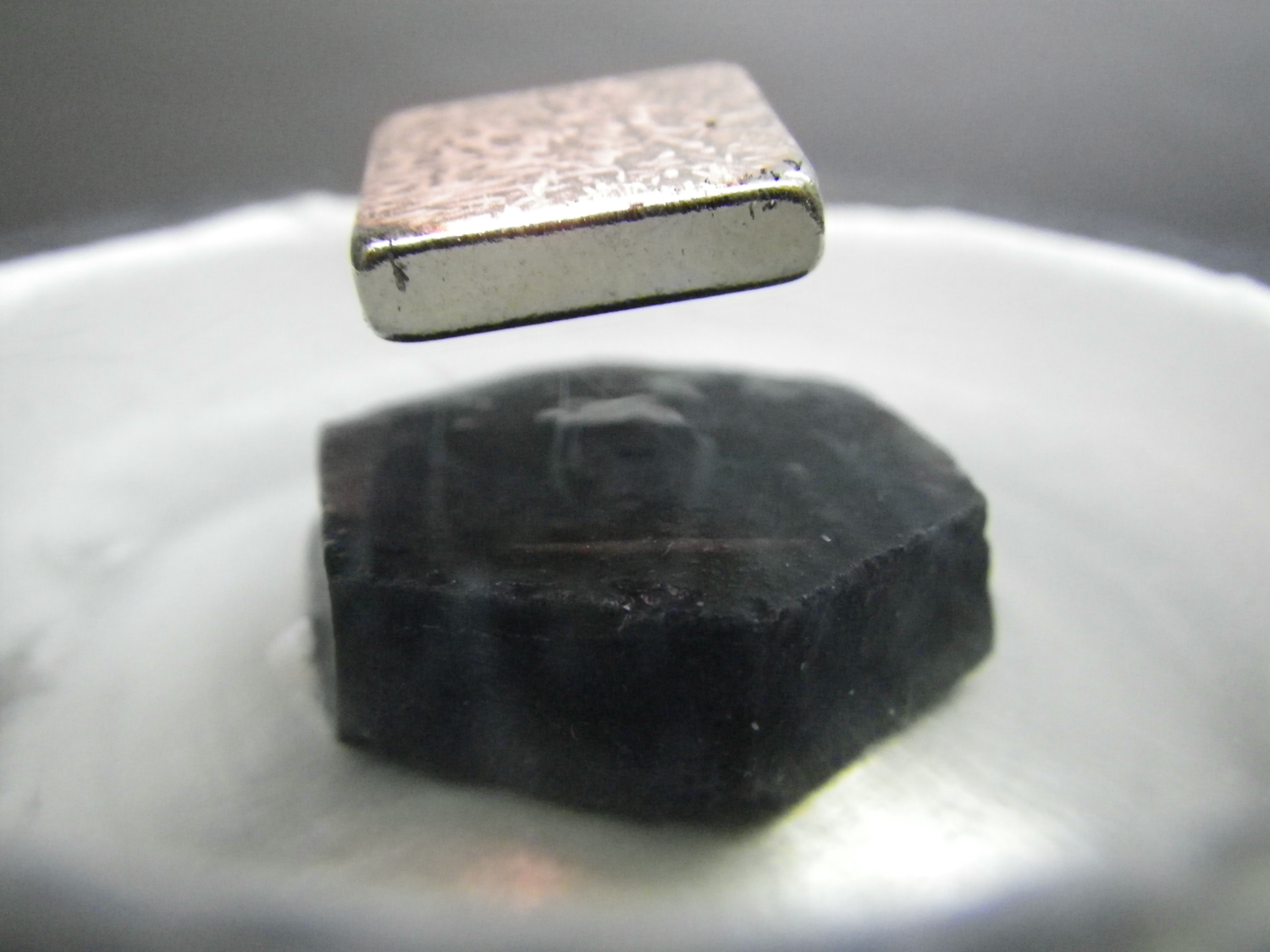 a square magnet levitating over a black chunck of supeconductive material sitting in a dish of liquid nitrogen
