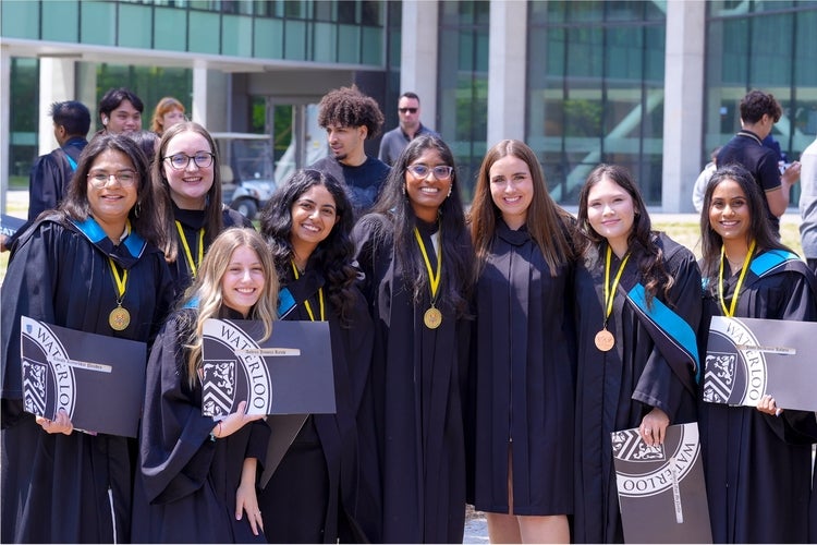 Eight graduates wearing convocation robes and holding their diplomas