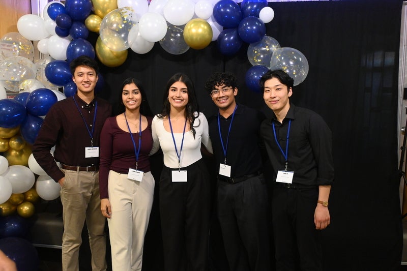 The winning team standing together against a black background with a blue balloon arch.