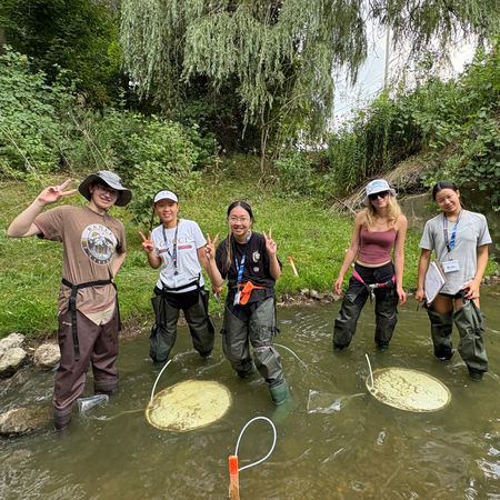 Five students conducting field work in a river in Vietnam.