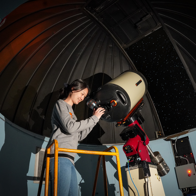 A physics student looking into a large telescope pointed at the night sky.