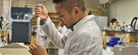 Male student pipetting in lab.