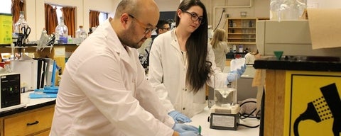 Male and female student in lab coats working in lab.