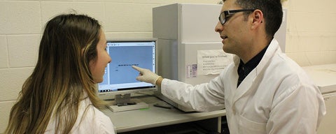 Male lab members points out data on computer screen to female student.