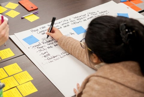 A photo of a student who is using a black marker to write onto a large piece of paper