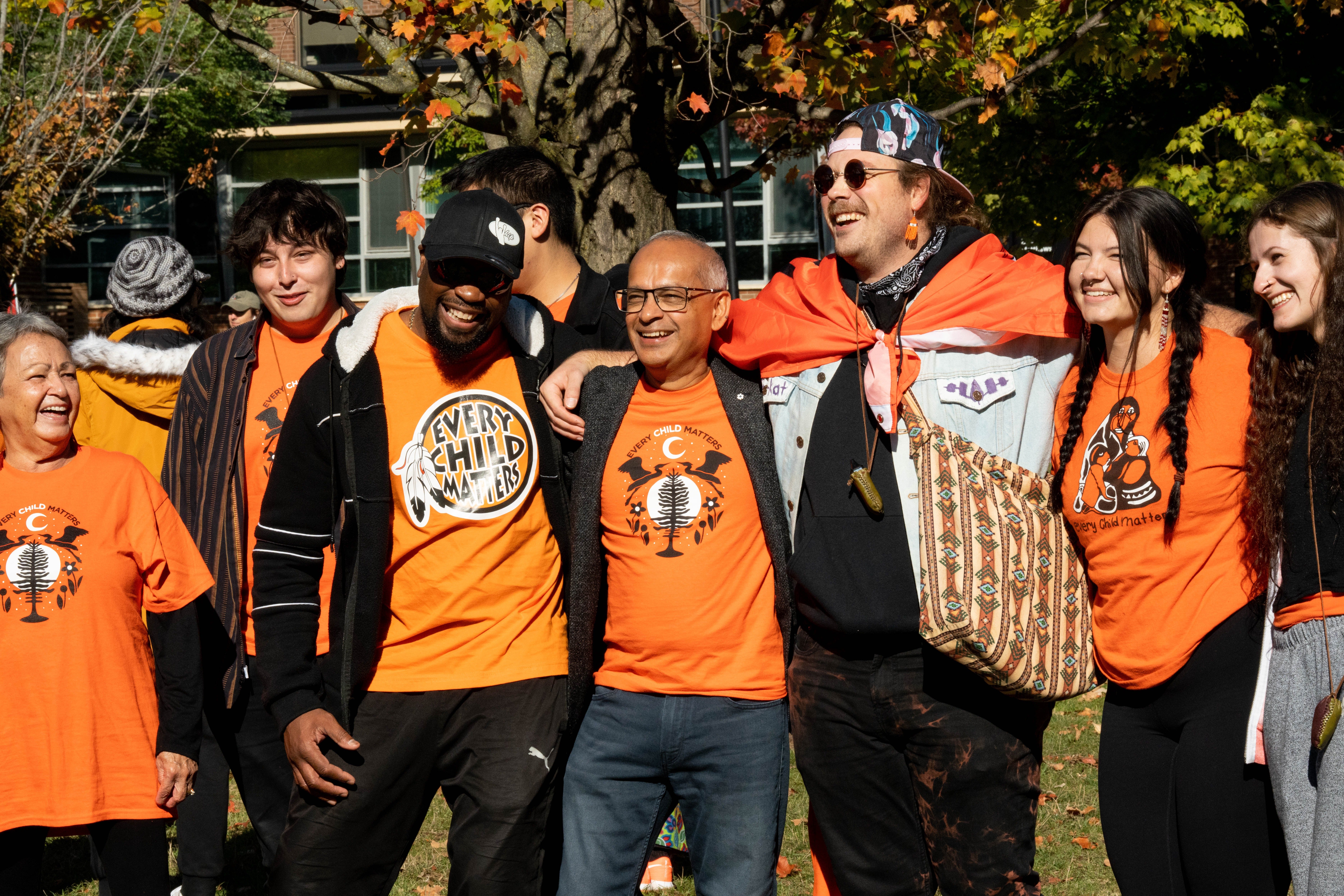 Vivek wearing an orange shirt with his arms linked around students wearing orange shirts