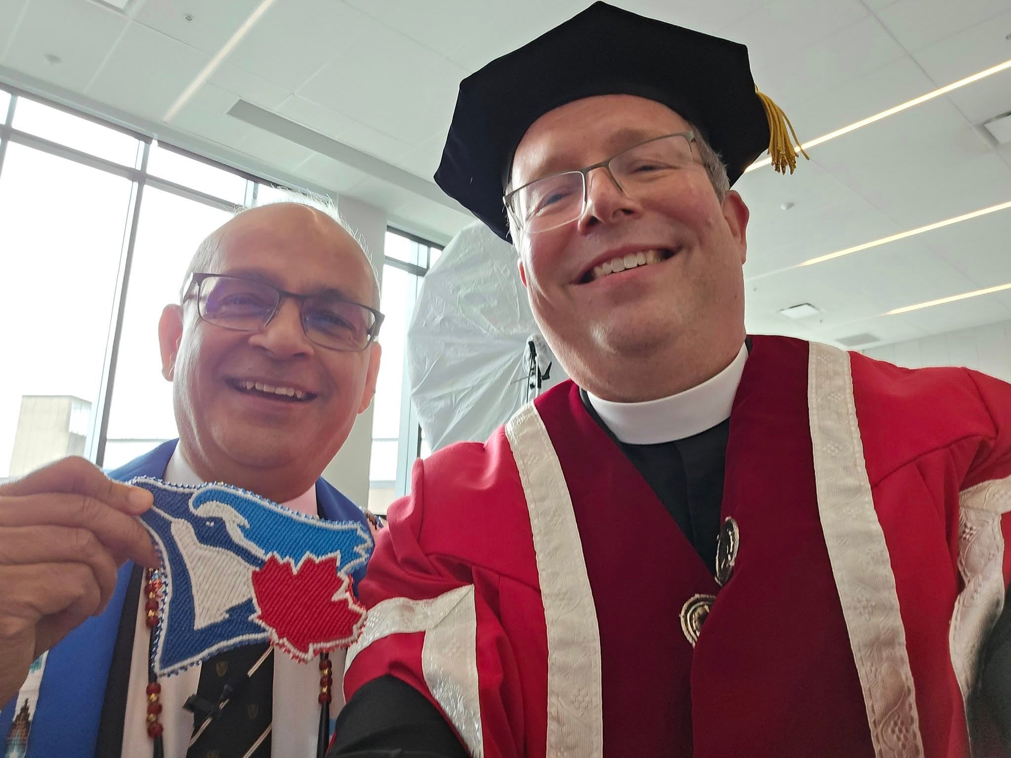 Vivek and Marc in formal academic regalia. Vivek is holding up a Blue Jays logo