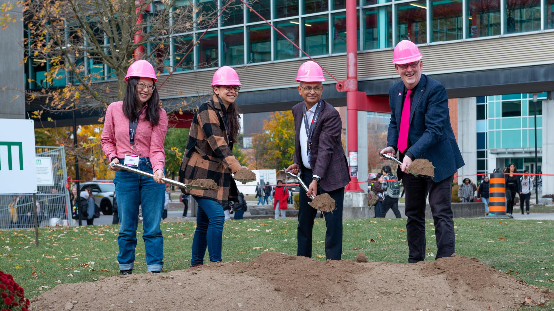 Four people with pink helmets ceremonially breaking ground
