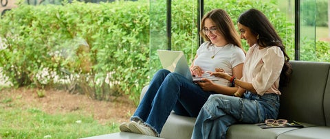 Two female University of Waterloo students looking at a laptop together on a sofa with greenery in the background