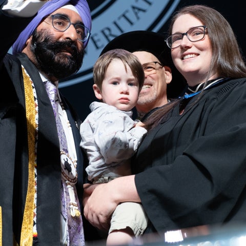 A graduate poses for a selfie with her child and faculty members on stage at convocation