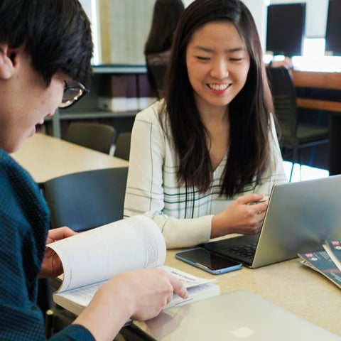 Waterloo male flipping through book and female student waiting to type on a laptop as they work together wearing business casual