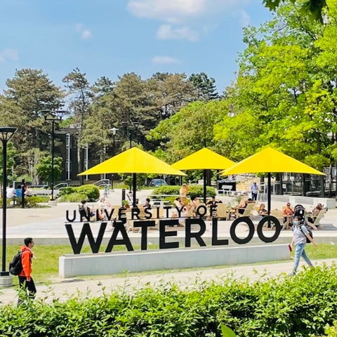 University of Waterloo signage with students walking across Arts Quad