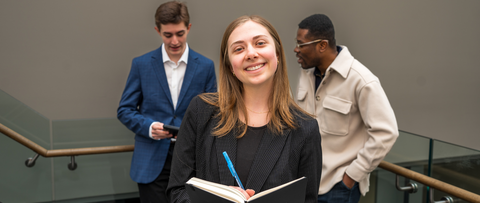 Female student holding a notebook and pen smiling in the foreground with two male co-op students wearing formal interview clothes in the background