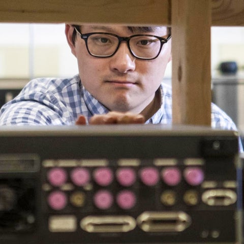 Dr. Adam Wei Tsen in the background controlling a technology device looking VHS