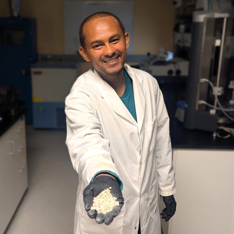 Researcher in a lab coat holding coated seeds