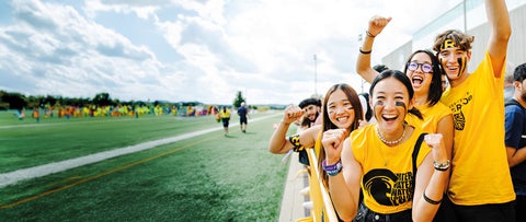 People stand beside a football field cheering together