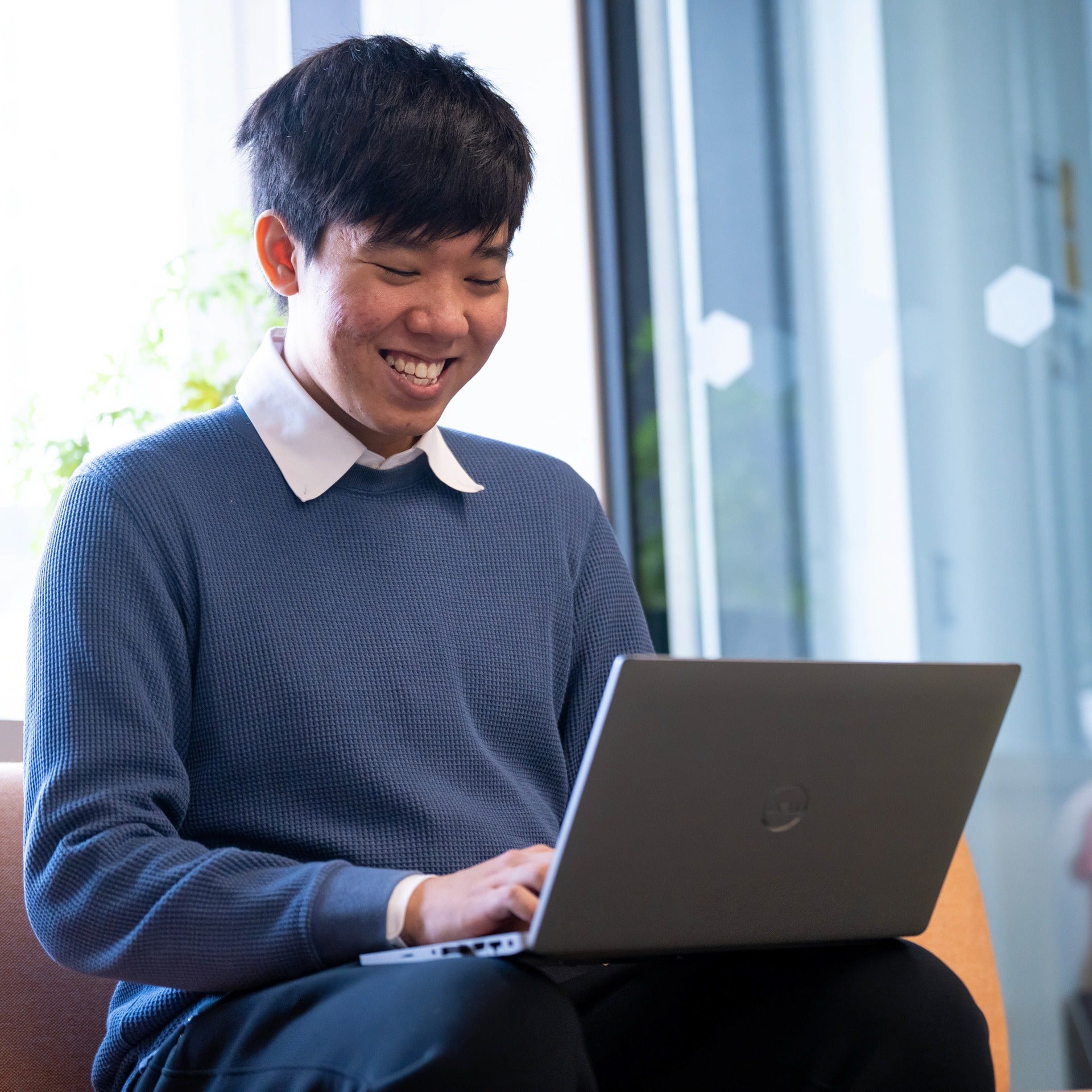 Hoang Do smiling and sitting with a laptop open on his lap