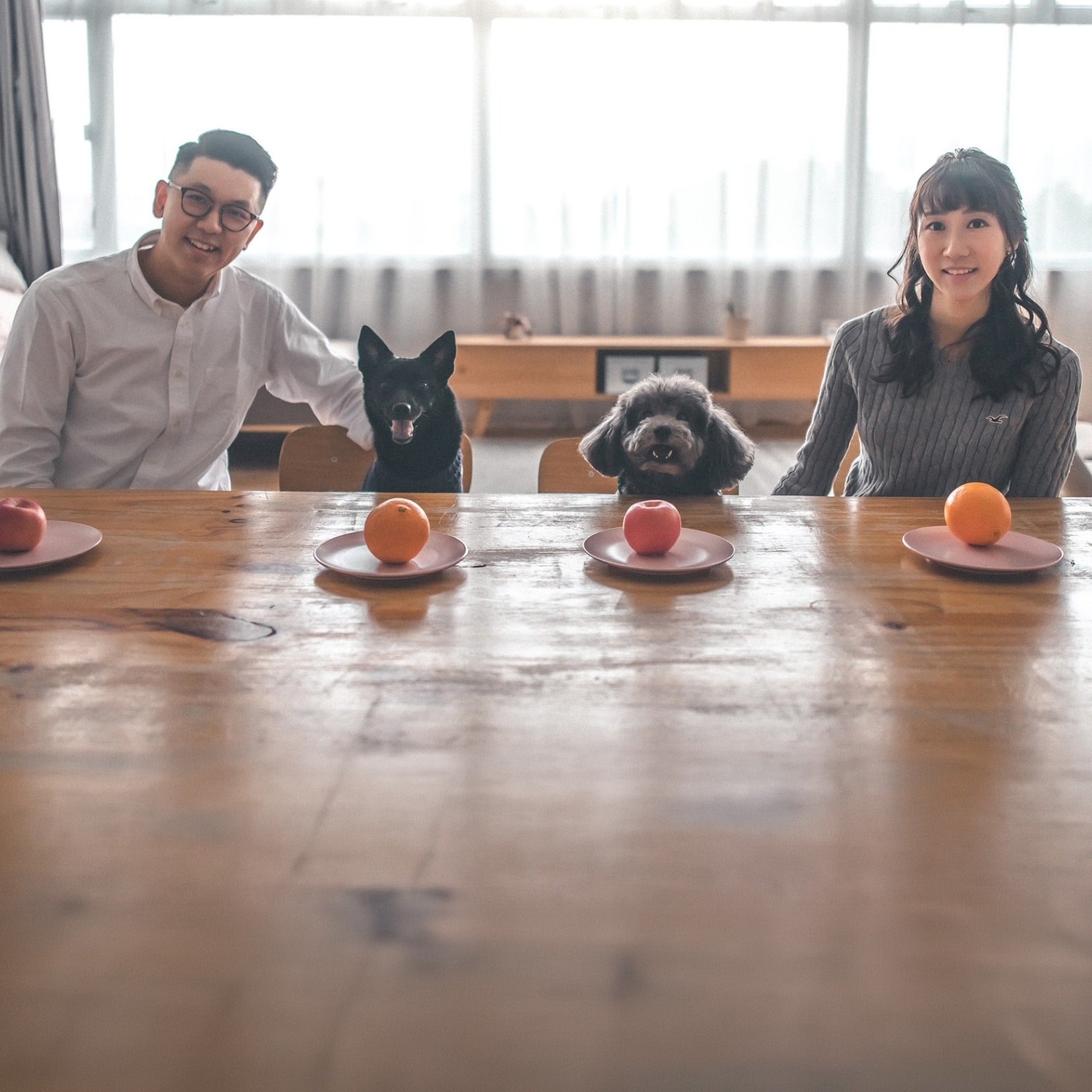 Emmanuel, Candy and their two dogs sitting with two oranges and one apple on top of plates on the table