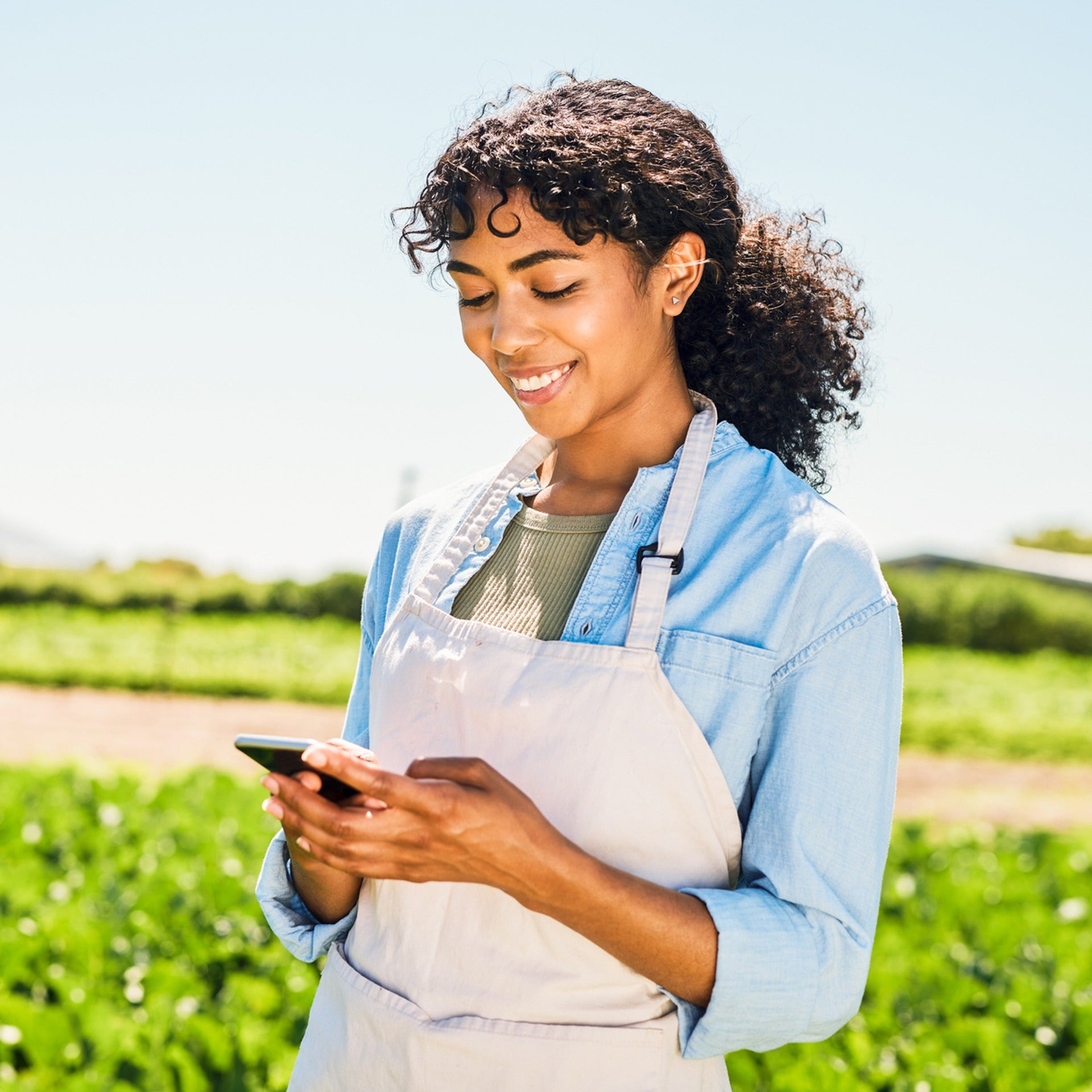 Woman wearing an apron using a mobile device in a remote farm area