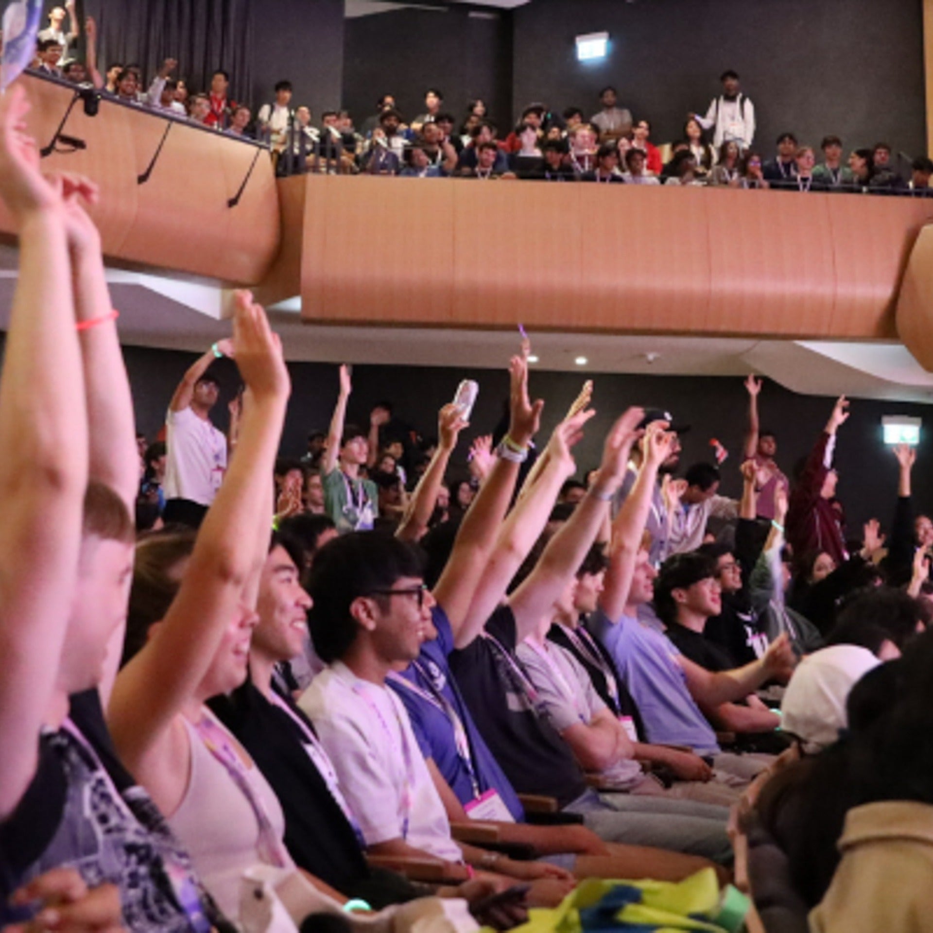 Students participating in Hack the North with their hands raised in the air sitting inside a theatre