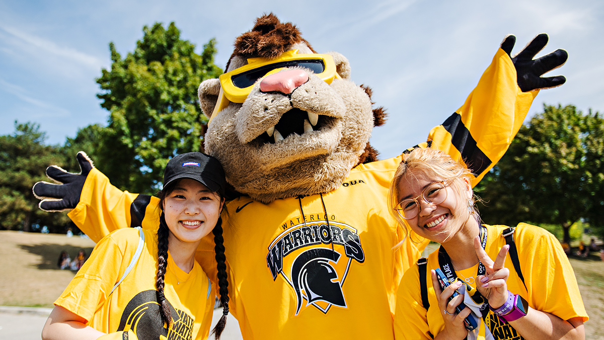 King Warrior mascot with two female students in Waterloo Warrior outfits 