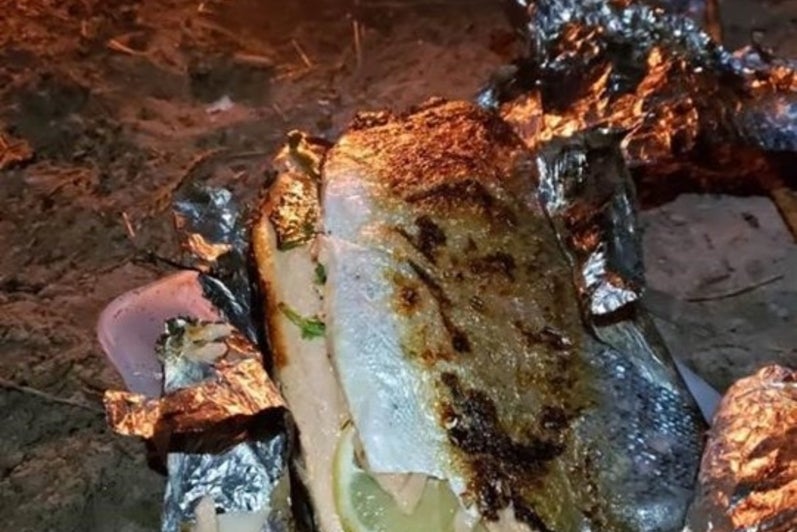 Picture of grilled fish in aluminum foil by a fire.