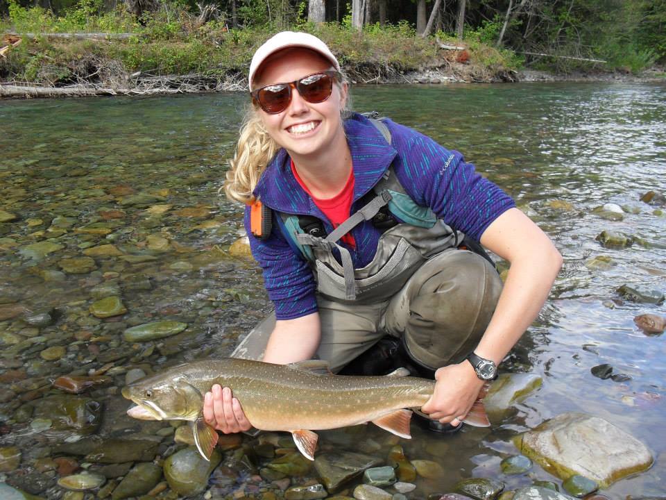 Cailey McCutcheon standing with waders in a river holding a fish