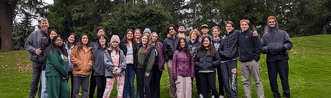 group of people standing together in a row smiling on green space