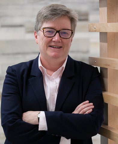 Catherine E. Clifford in a suit jacket and white blouse. smiling in front of a brick and white wall