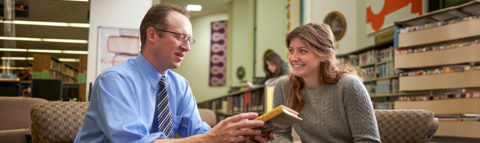 Professor Chad Wriglesworth speaks with a student while holding a book he authored