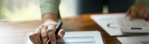 Person looking over financial documents with a pen in their hand