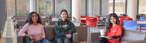 Three students sip coffee and socialize in the Ryan and Siegrfried Hall lounge.