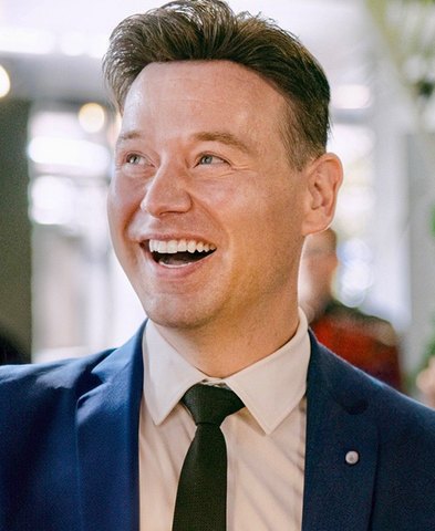 Matthew Durham smiles in a suit jacket and tie