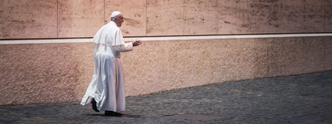 Pope Francis walking in front of a white wall