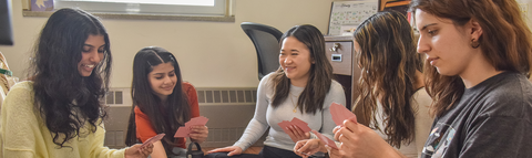 4 students play cards in a single bed room in J.R. Finn and Siegfried Hall Residence