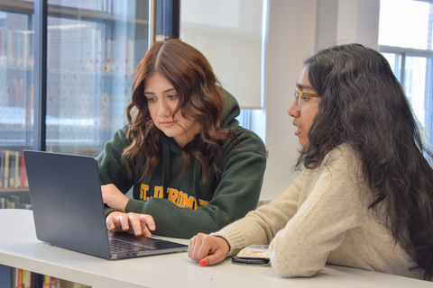 Two students study together at a table in the library